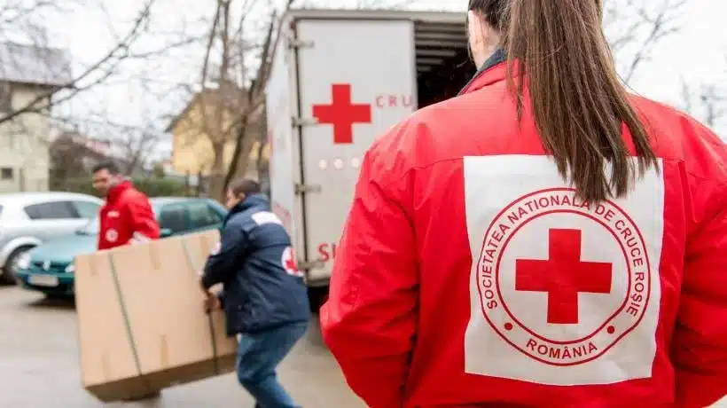 Voluntari de la Crucea Roșie Română descărcând ajutoare dintr-un camion.